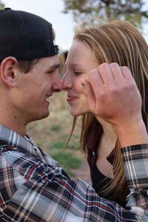 A young couple in plaid shirts lean in close for a kiss outdoors at dusk.