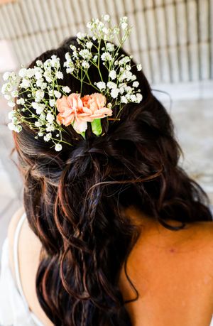 Bride with dark wavy hair adorned with baby's breath and peach carnation flowers.