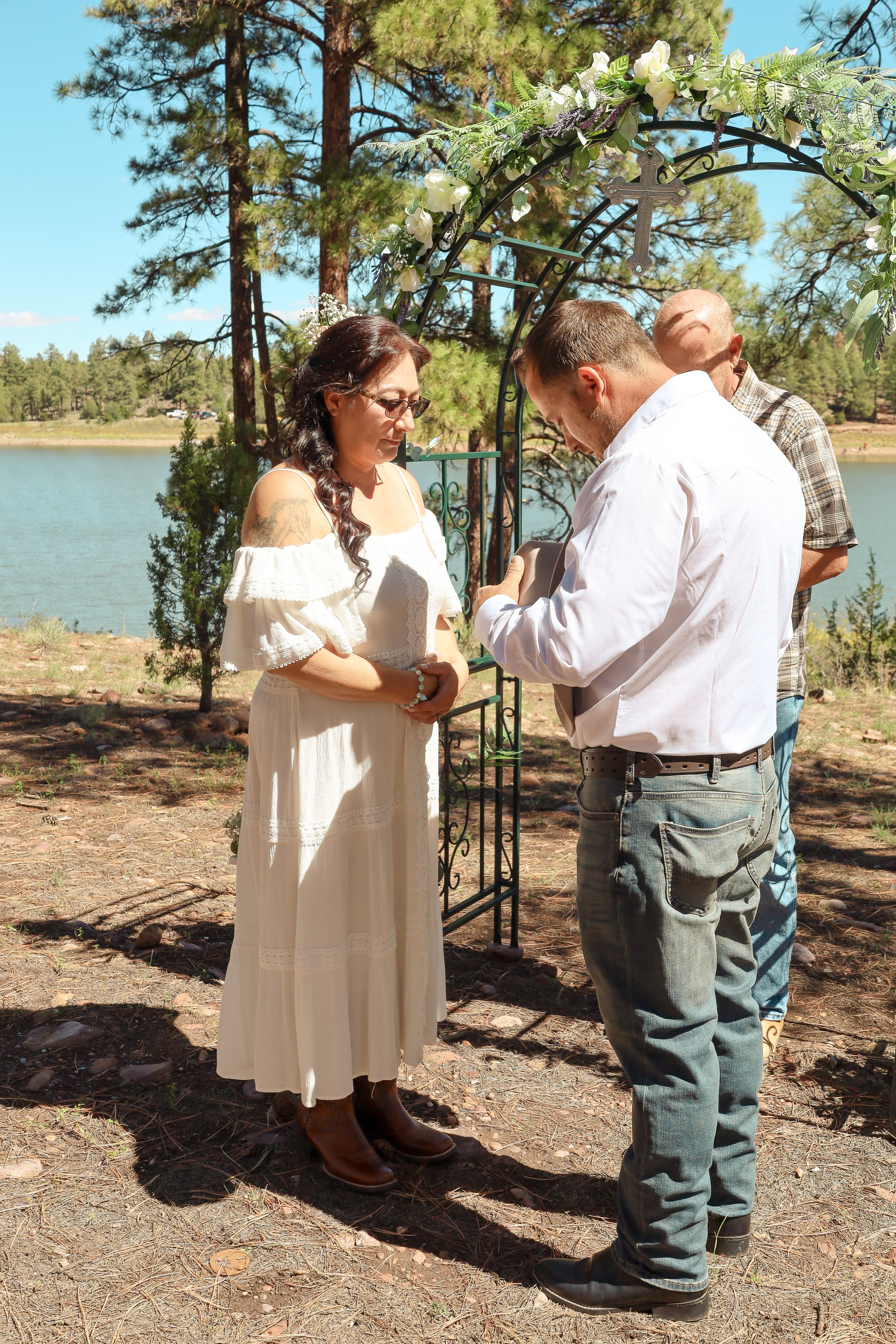 Bride and groom exchange vows under floral arch by lakeside wedding ceremony.