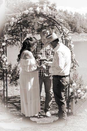 Black and white photo of bride and groom exchanging rings at outdoor wedding.