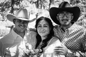 Black and white portrait of bride with two men in cowboy hats at wedding.