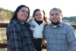 Happy family of three with young child posing together outdoors near a wooden fence.