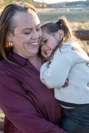 Joyful grandmother cuddling her smiling granddaughter outdoors in warm afternoon sunlight.