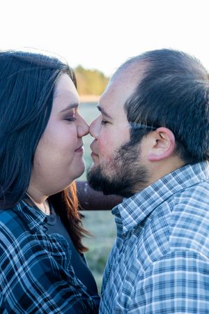 Romantic couple sharing a kiss outdoors in soft natural light during a family photo session.