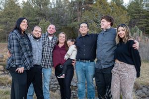 Large extended family group smiling together outdoors in a natural wooded setting at dusk.