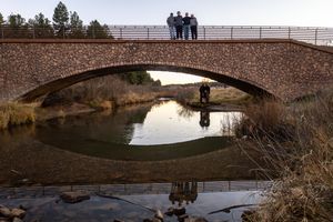Family posing on a stone arch bridge reflected in calm river water below at golden hour.