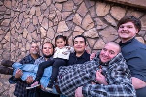 Happy family group smiling together against a stone wall backdrop in warm indoor lighting.