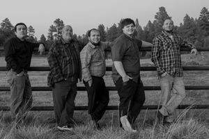 Black and white photo of five men leaning against a wooden fence in a rural field.