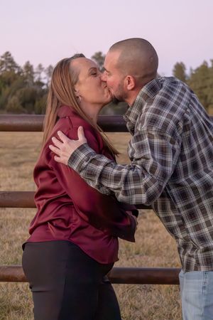 Couple sharing a romantic kiss by a rustic wooden fence in an open field at dusk.