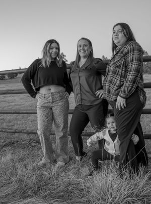 Black and white photo of three women and a toddler posing by a wooden fence at dusk.