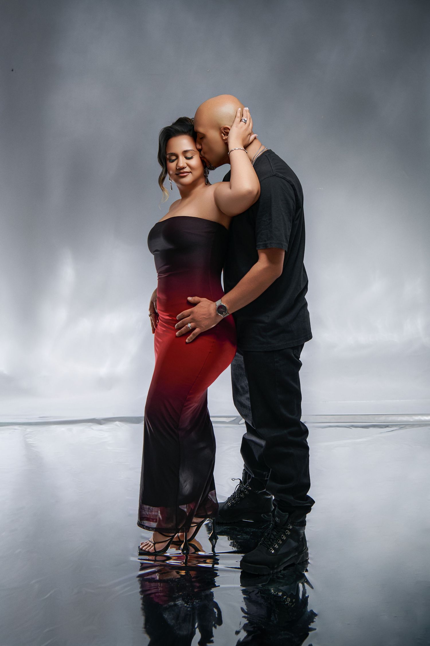 Couple in intimate dance pose against gray backdrop, with woman in ombre dress and man in black attire.