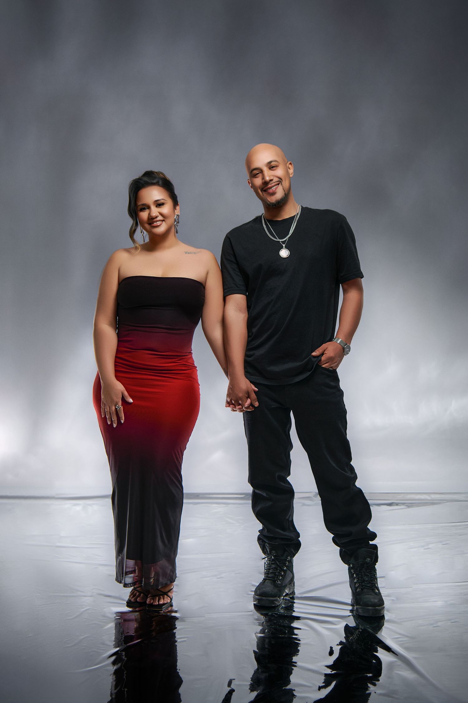 A couple poses together on reflective surface wearing black and red gradient dress and all-black casual outfit.