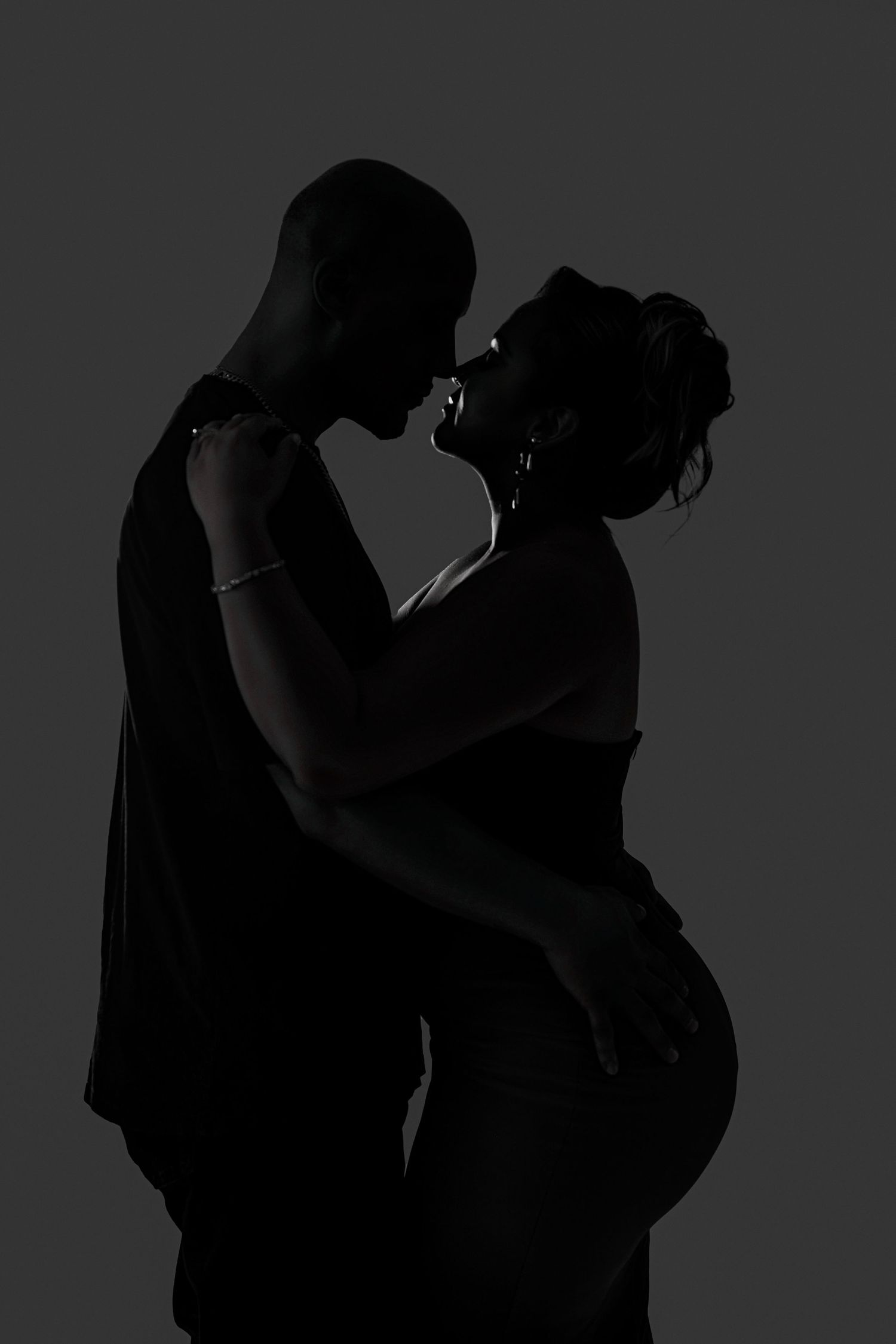 Silhouetted couple in an intimate embrace against dark background creates dramatic romantic mood.