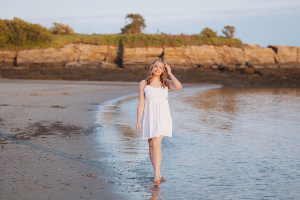 A barefoot person in a white dress walking along the shoreline at sunset creating a peaceful coastal scene.