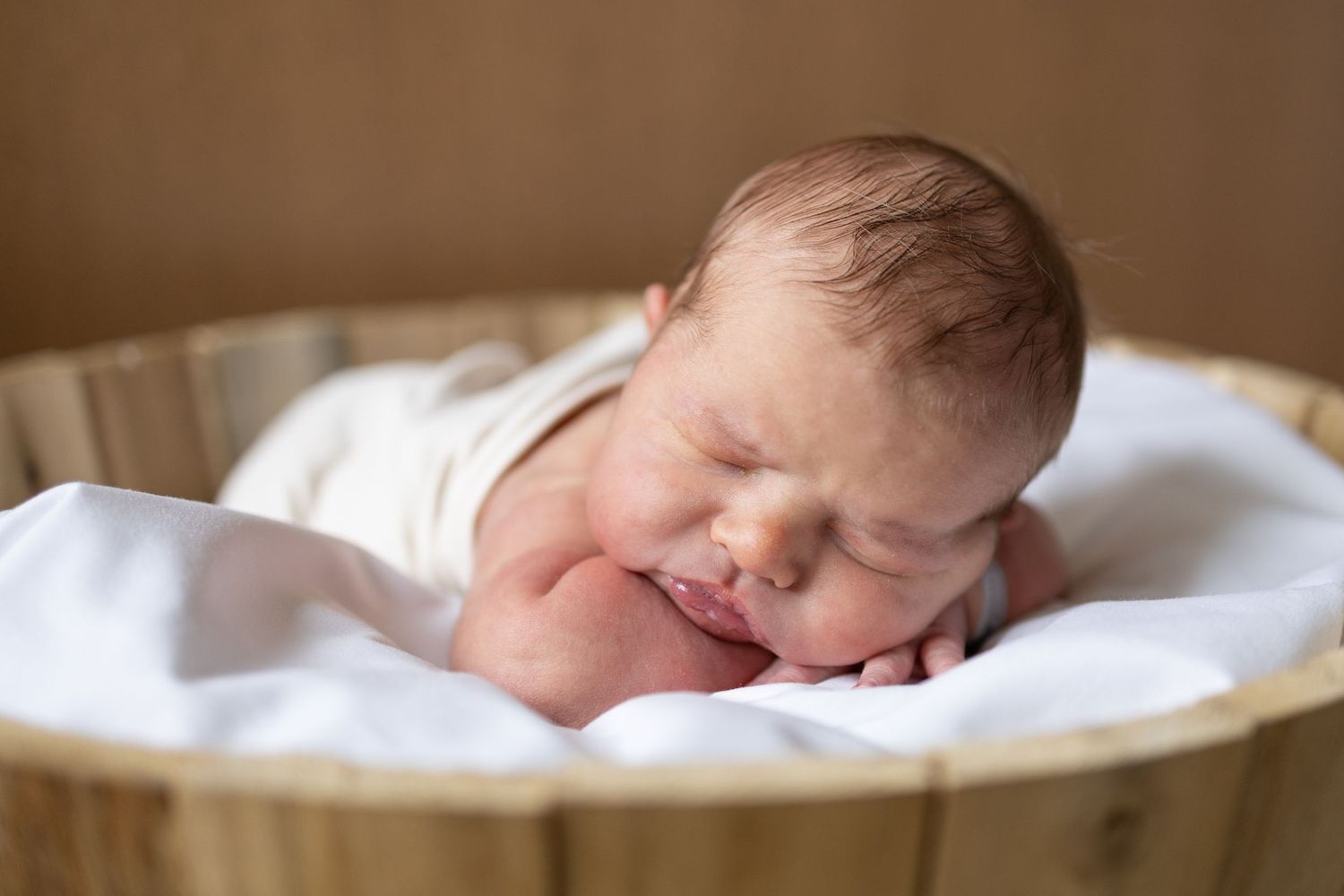 Peaceful newborn baby sleeping soundly on soft white blanket in wooden basket. Newborn pose.
