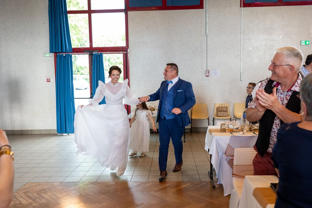 A couple makes their grand entrance at a wedding reception in a bright community hall.