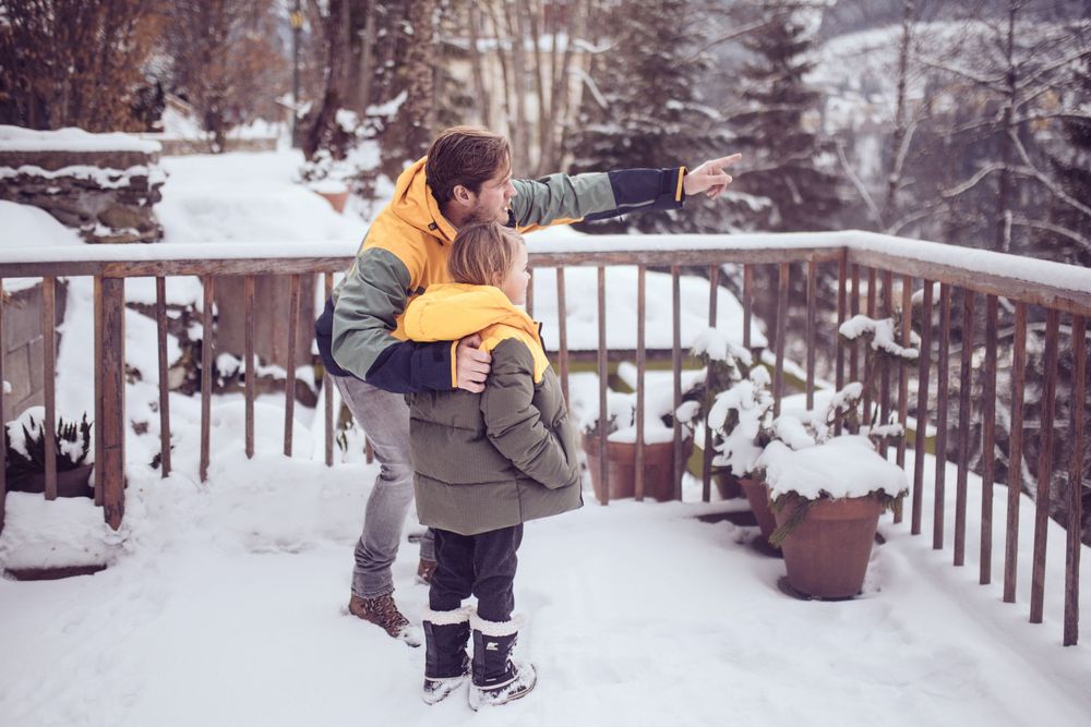Couple embraces on snowy deck with winter mountain landscape in background.