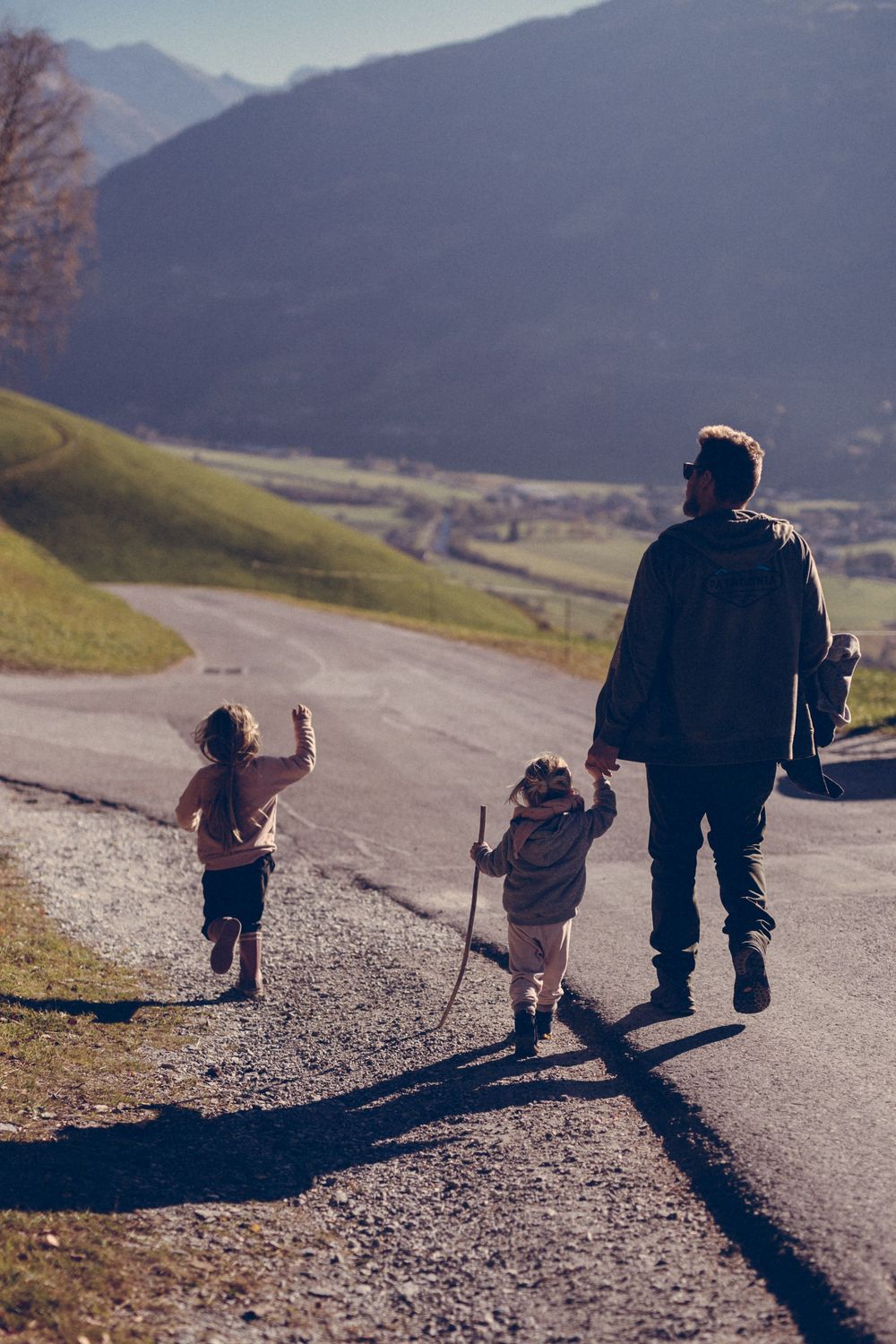 A family goes hiking together on a mountain path on a sunny day with mountains and valleys in the background.