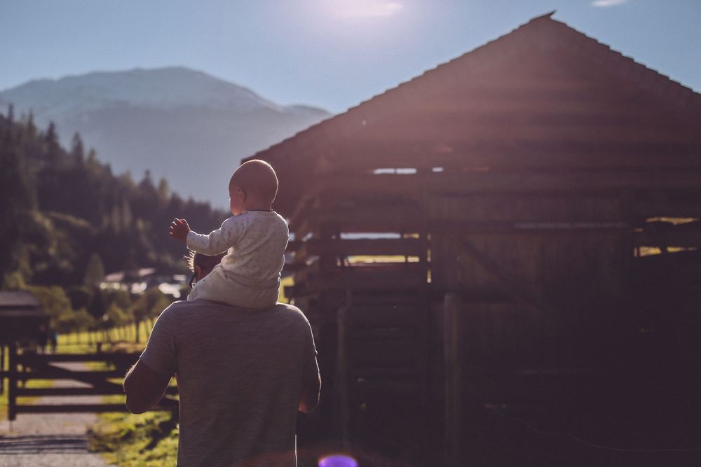 Silhouette of parent and child looking at mountain landscape near wooden structure during sunset.