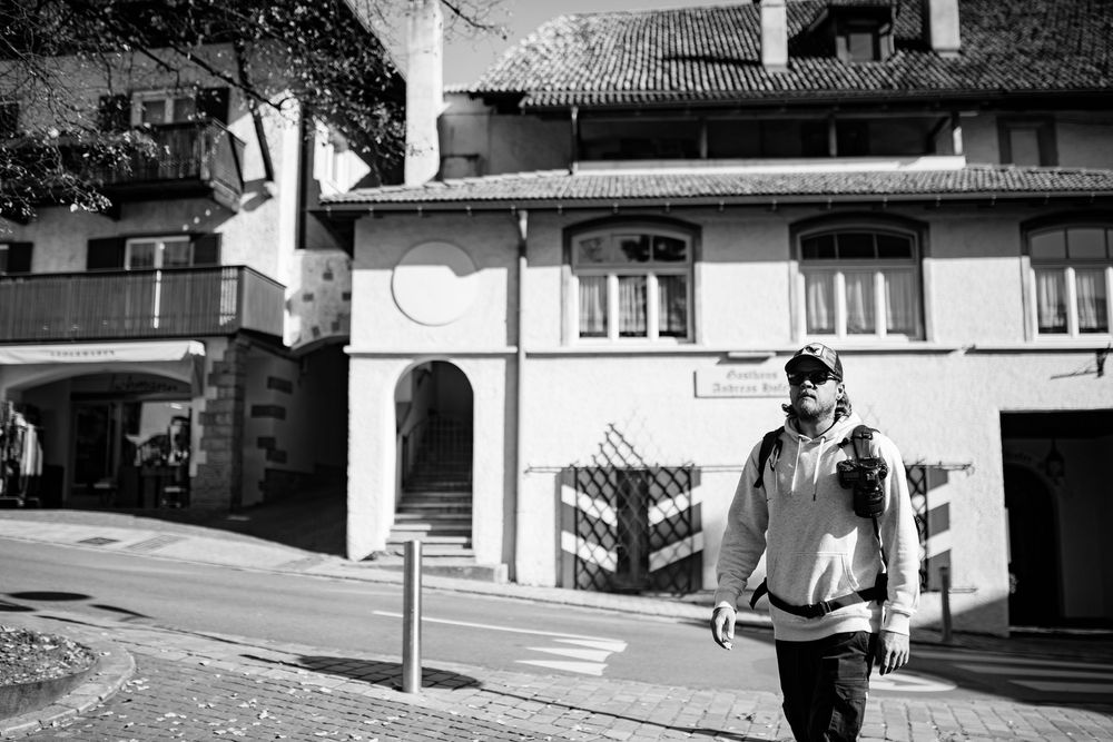 Figure walking past historic building on cobblestone street in black and white.