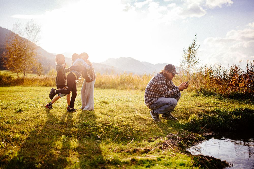 Group taking photos in sunlit mountain meadow during golden hour.