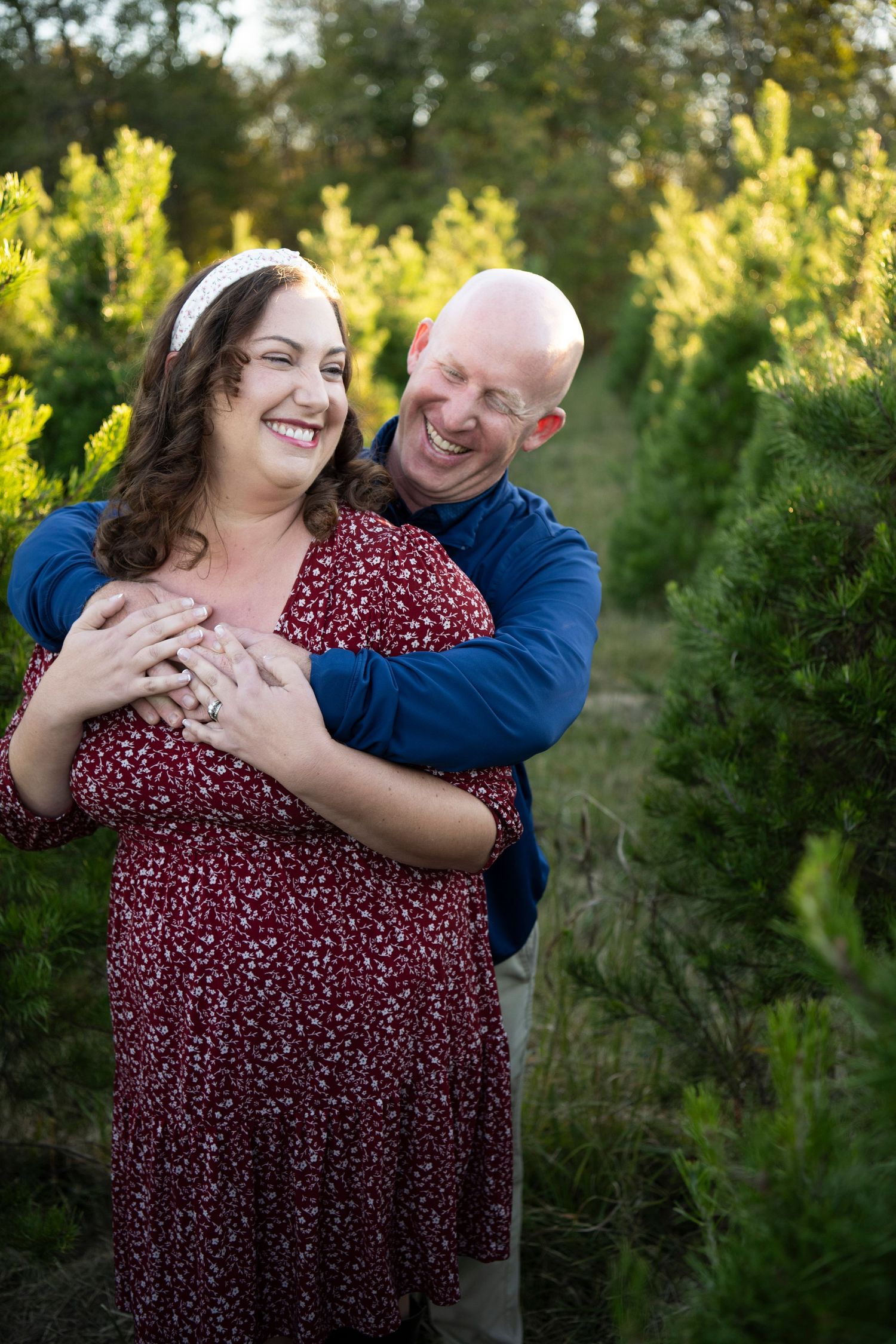 Couple sharing a candid laughing moment among evergreen trees at golden hour in Columbia, TN.