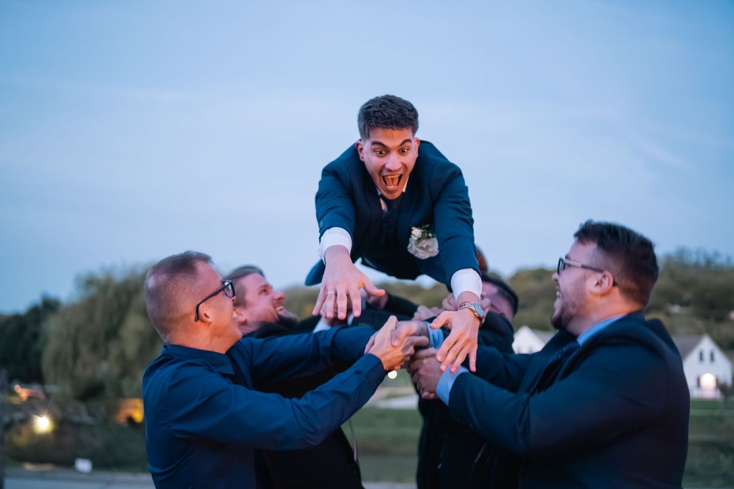 Three people in dark jackets playfully celebrating and raising beverages together at dusk while enjoying an outdoor gathering.