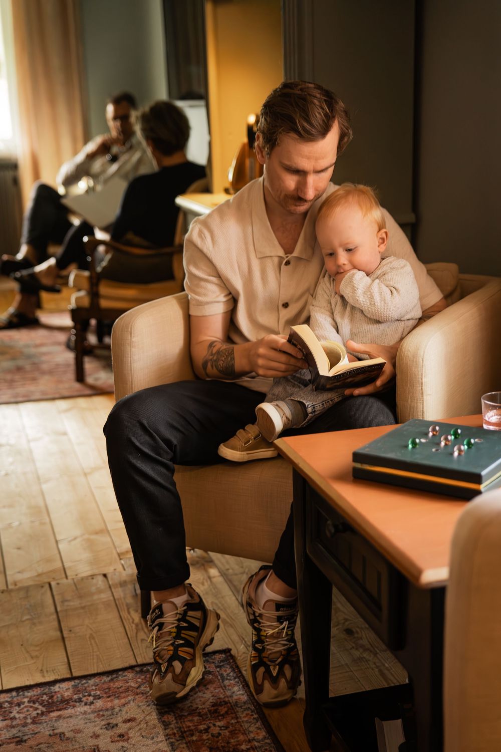 A quiet reading moment in a warmly lit living room with comfortable armchairs and wooden flooring.
