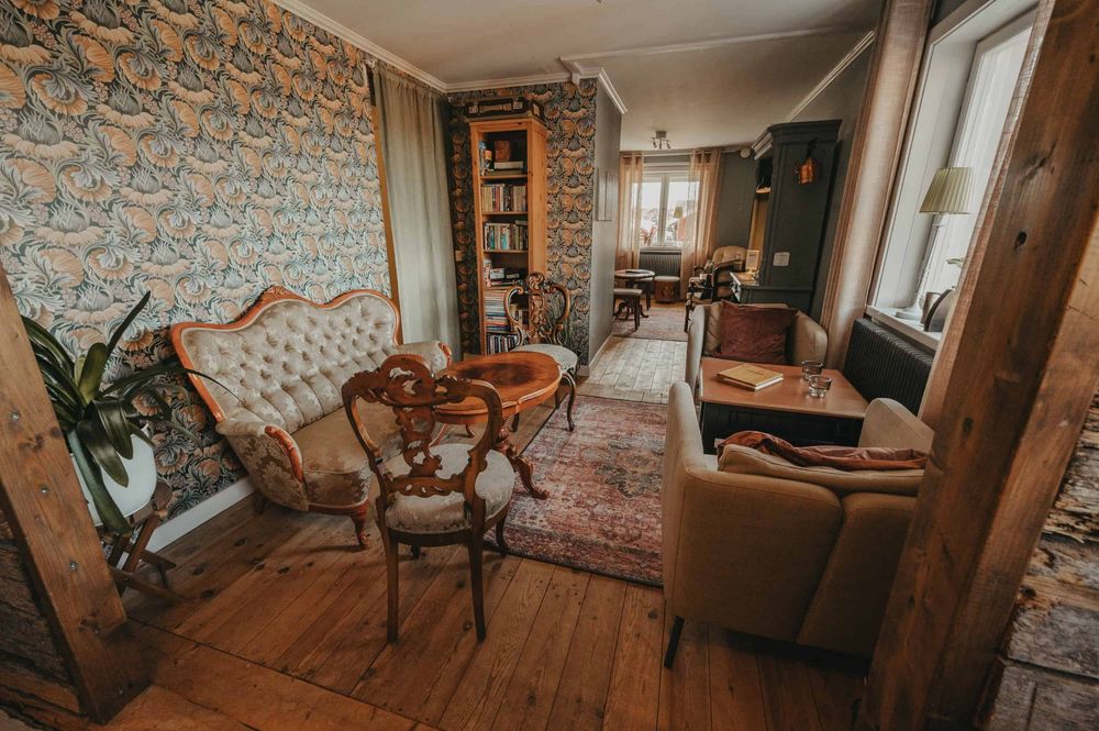 A cozy vintage-style living room with floral wallpaper, wooden floors, and antique furniture creates a warm atmosphere.