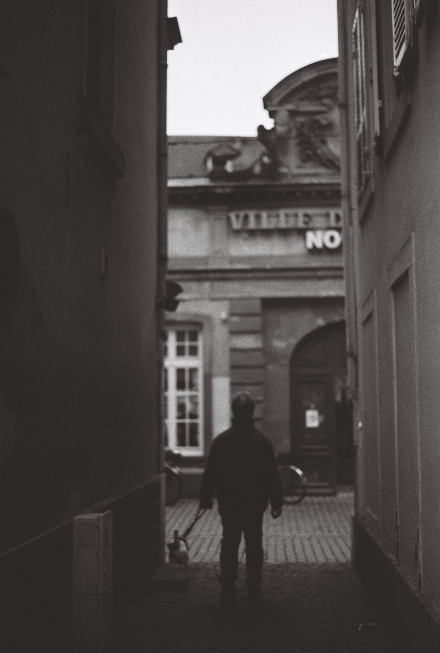 Silhouette of person walking through narrow alley between old buildings.
