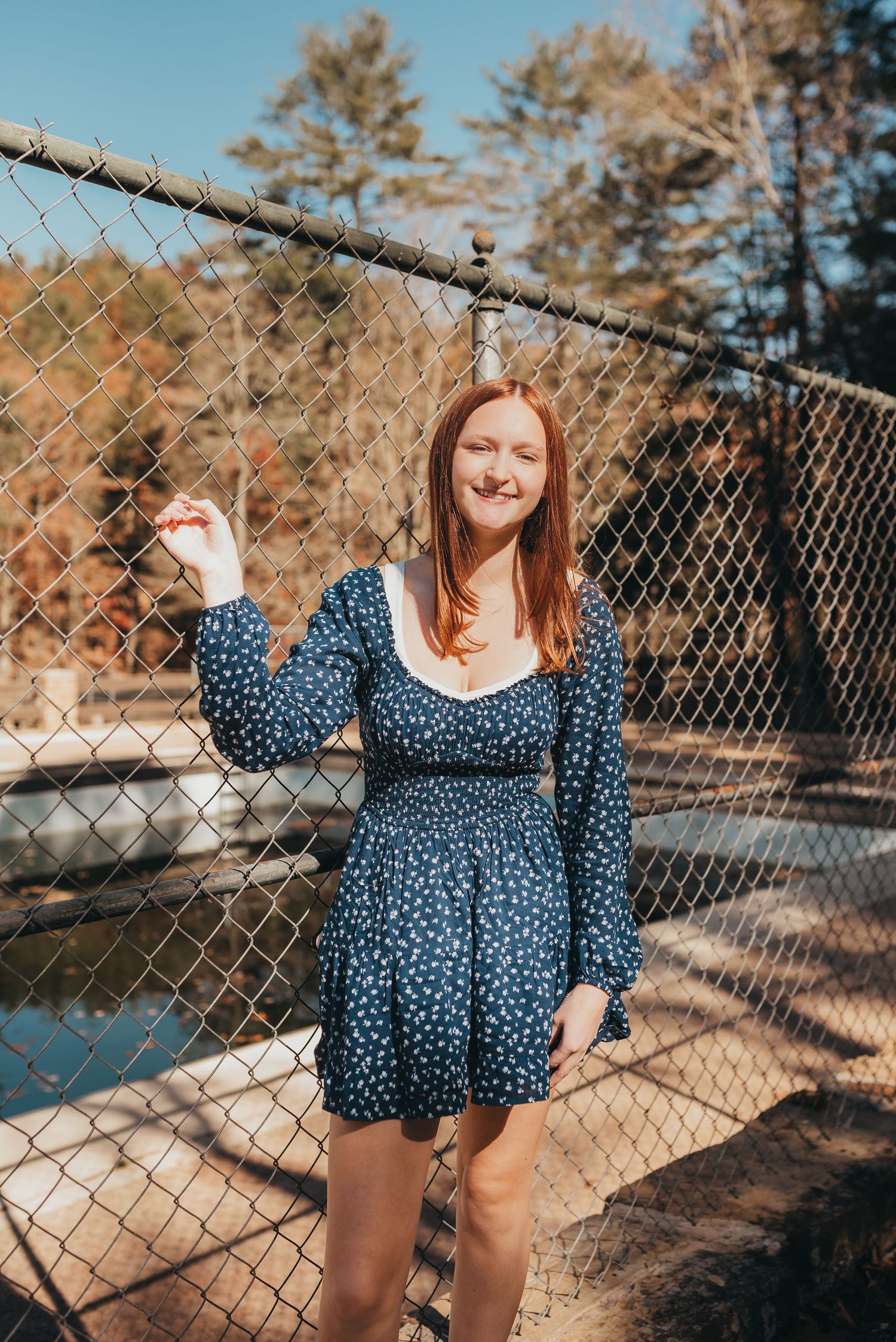 A joyful pose by a chain link fence wearing a blue polka dot dress.