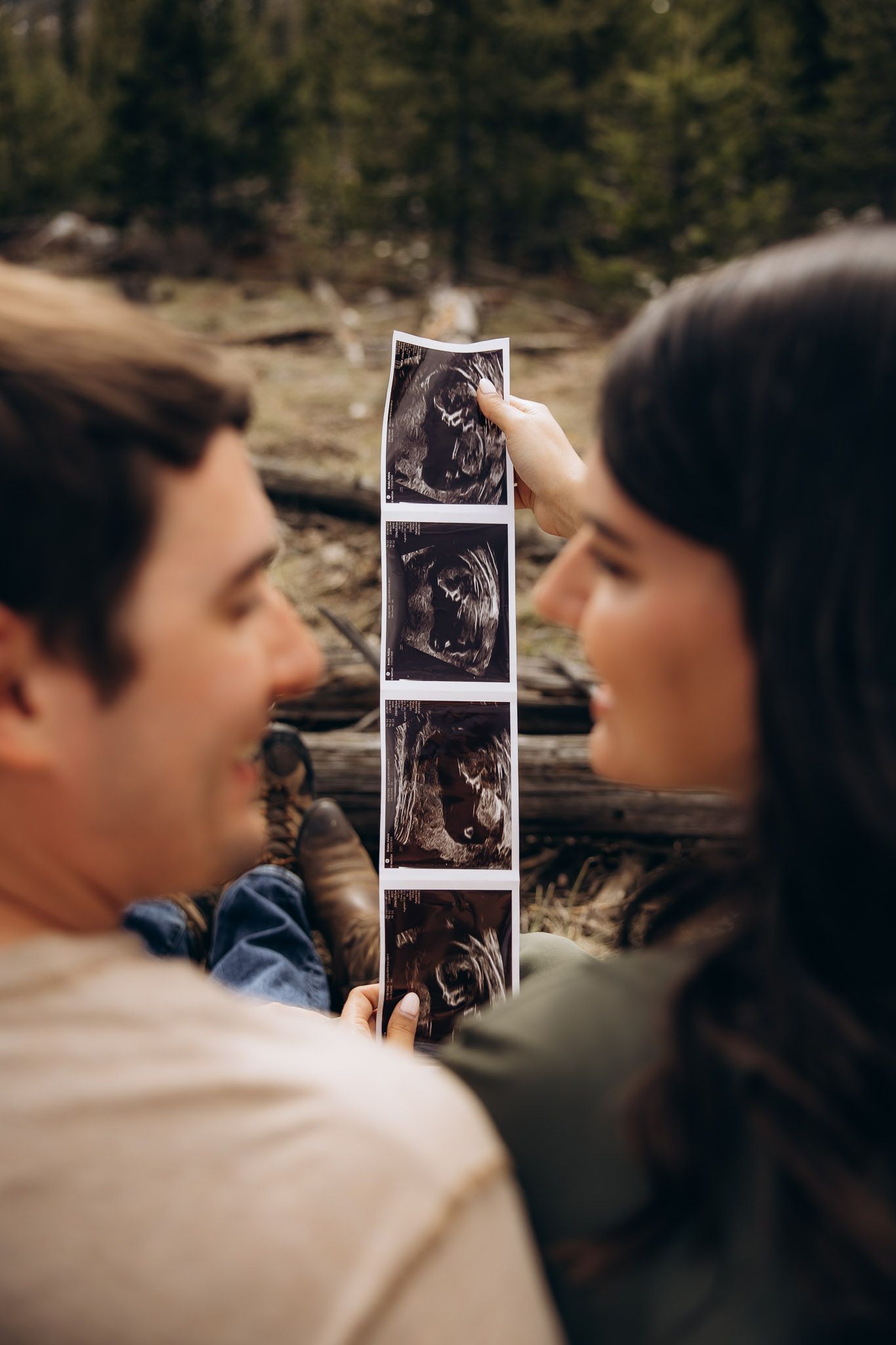 A couple holds up an ultrasound strip showing four images of their expected baby against a blurred outdoor background.