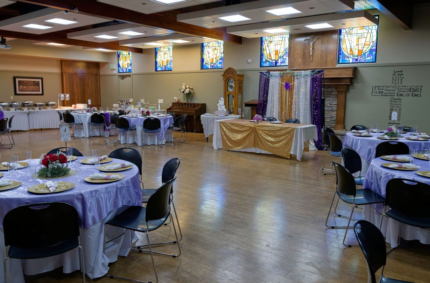 A couple walks down a church aisle decorated with a red carpet and floral arrangements on the wooden pews.