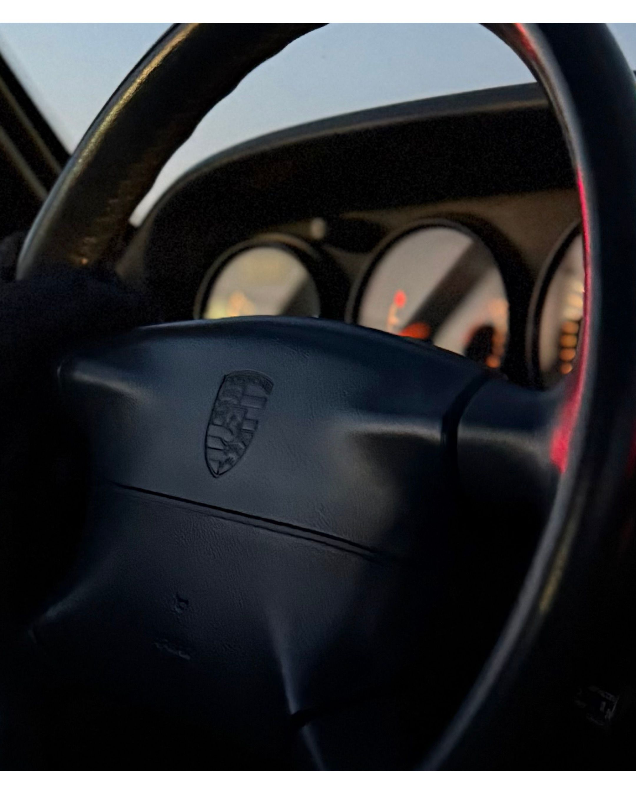 Close-up of a black Porsche steering wheel in dim lighting.