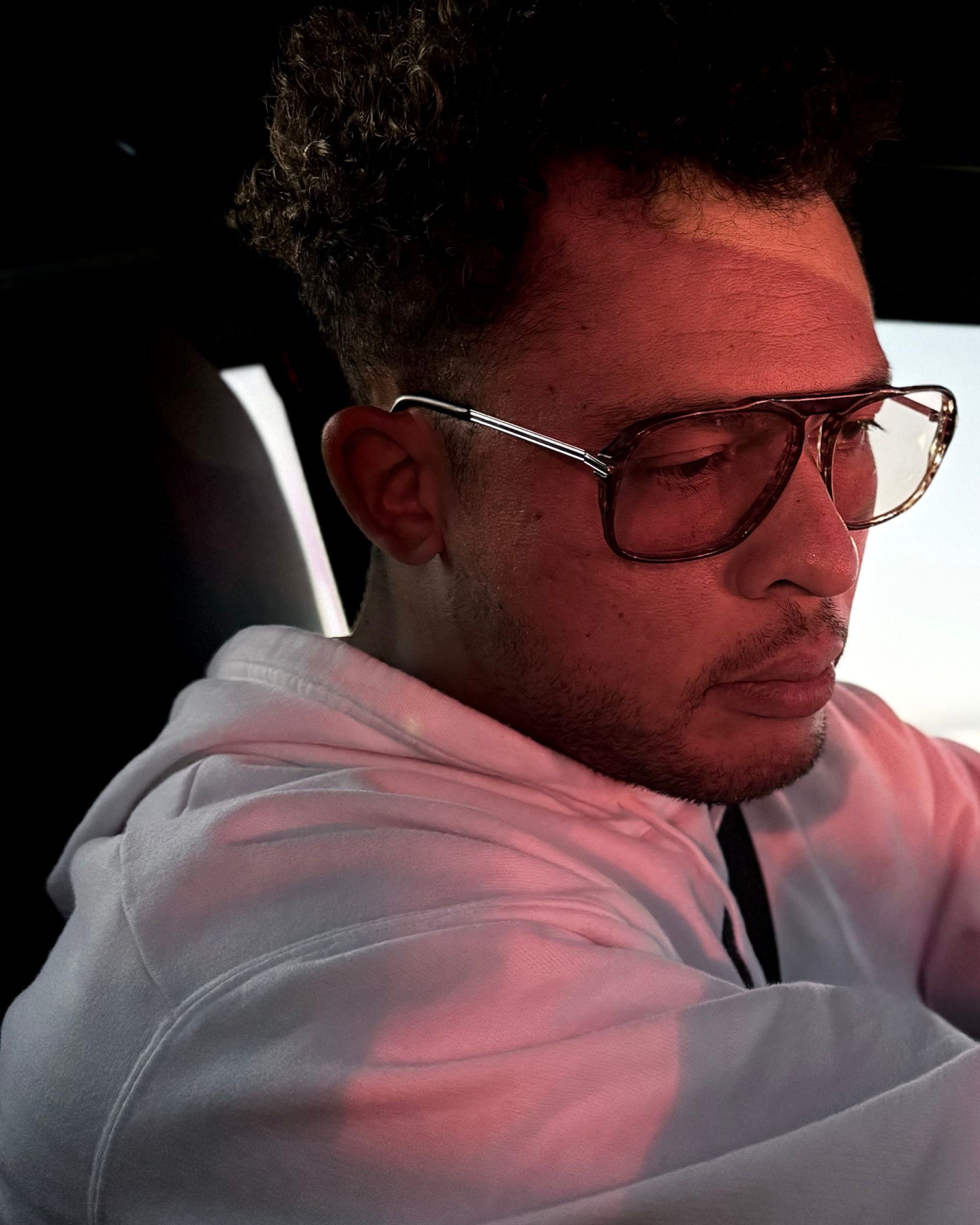 Portrait showing a person wearing glasses and pink hoodie in a car.