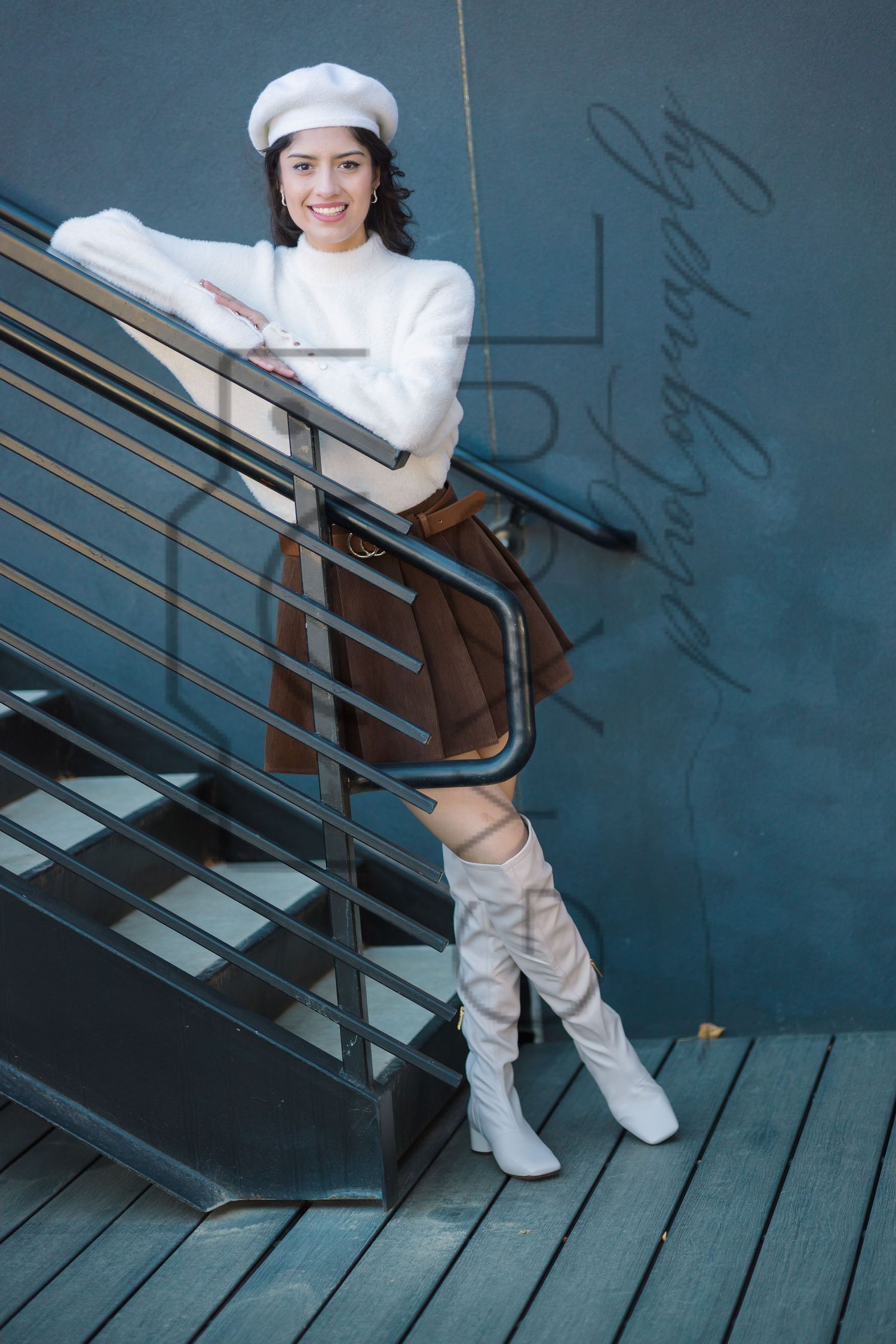 A person in a white sailor-style outfit with tall boots poses on dark wooden stairs against a blue wall.