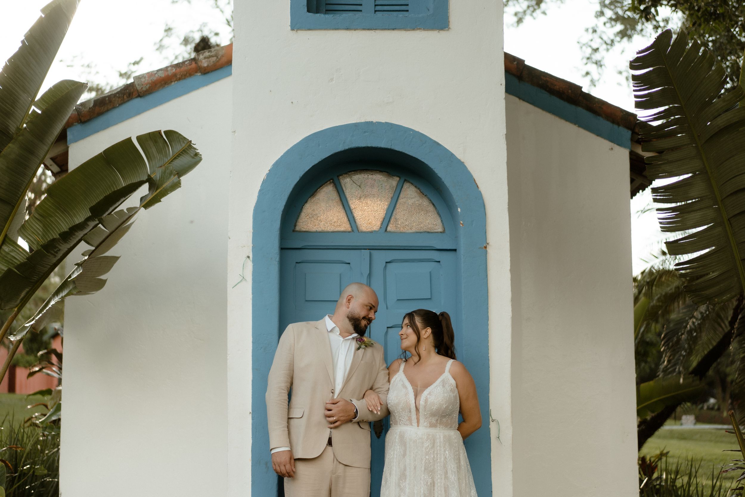 Wedding couple posing by charming white chapel with blue arched doorway.