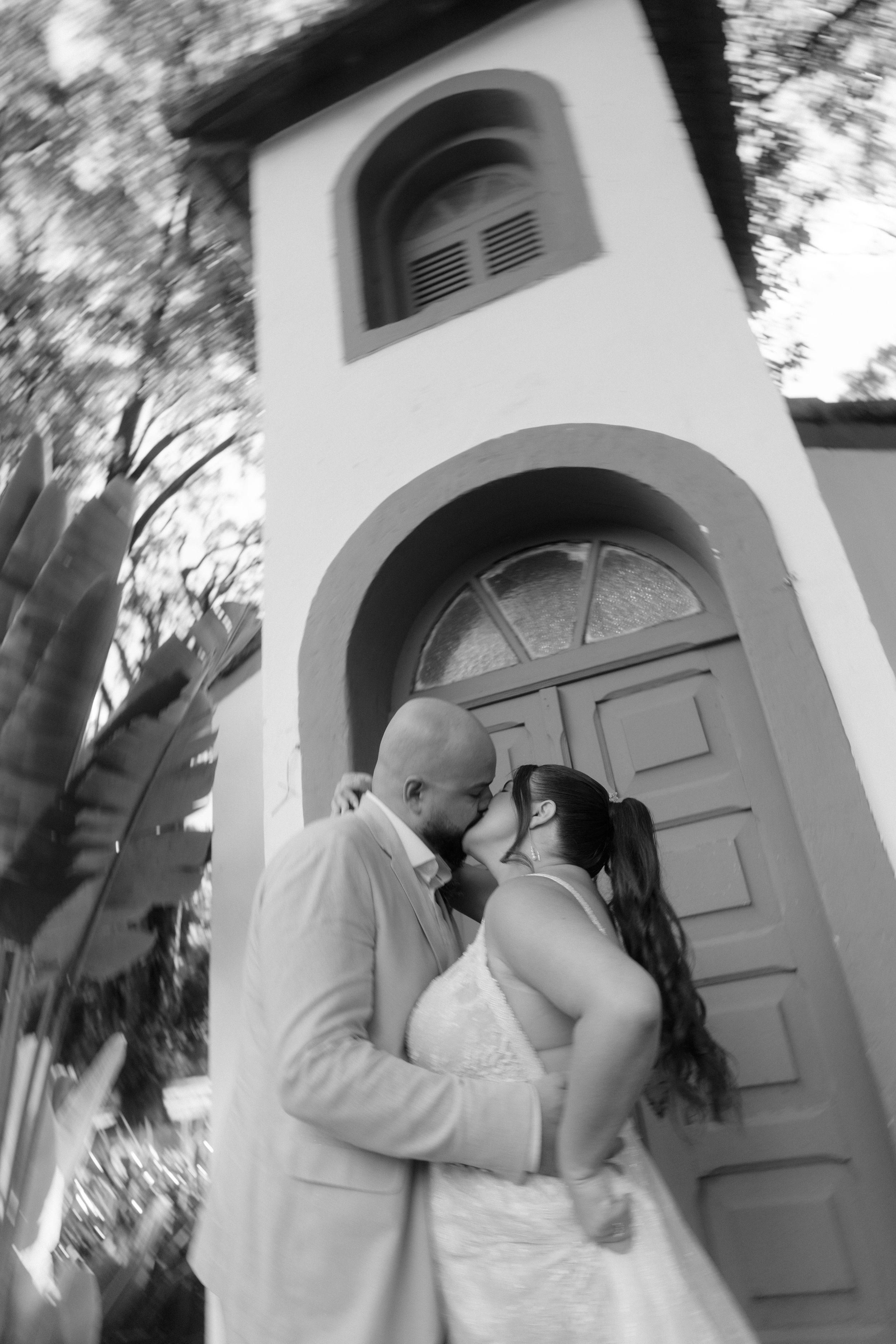 Black and white wedding portrait of couple embracing by vintage church entrance.