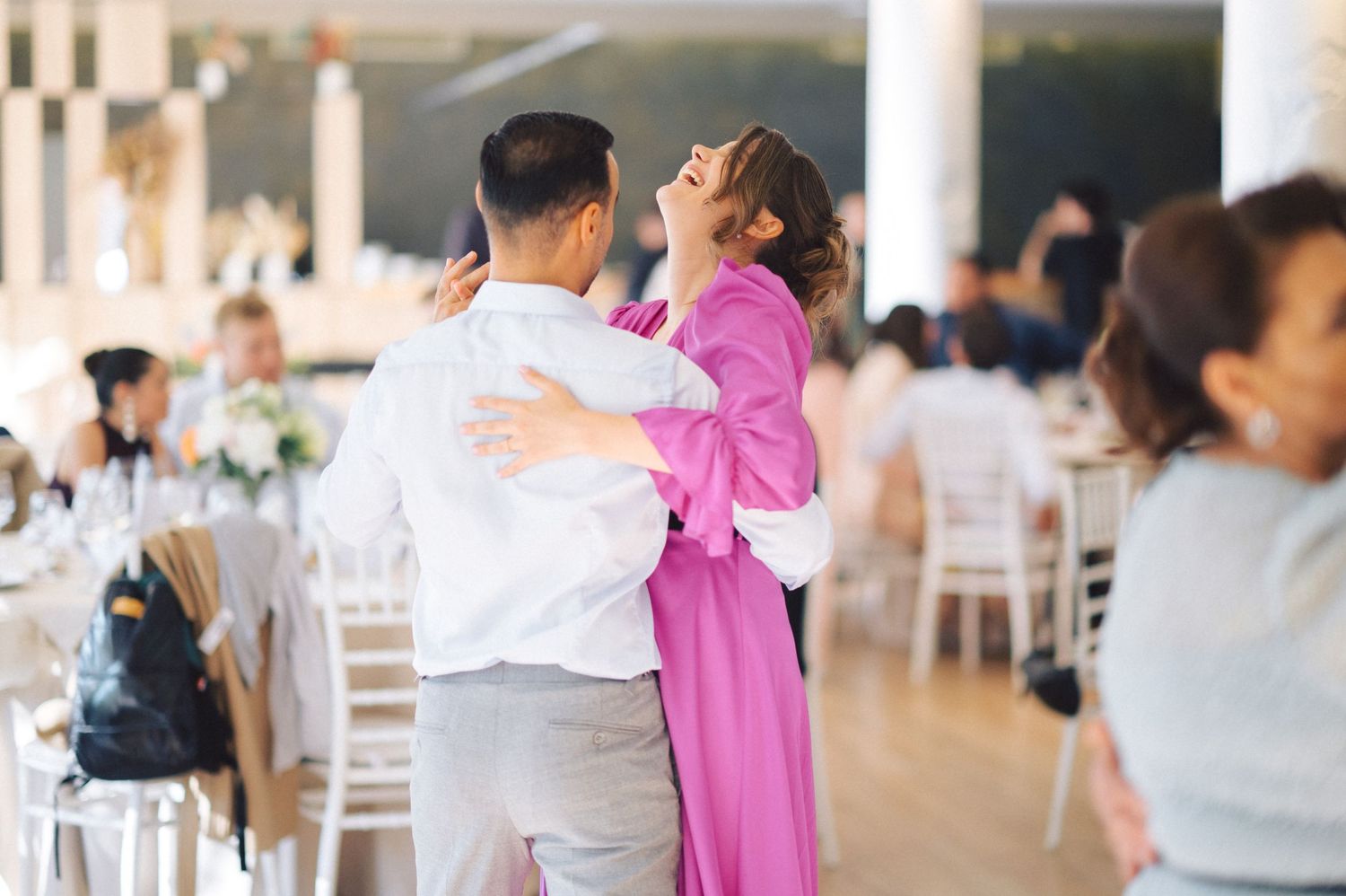 A couple dancing together at an elegant wedding reception with white chairs and tables in the background.