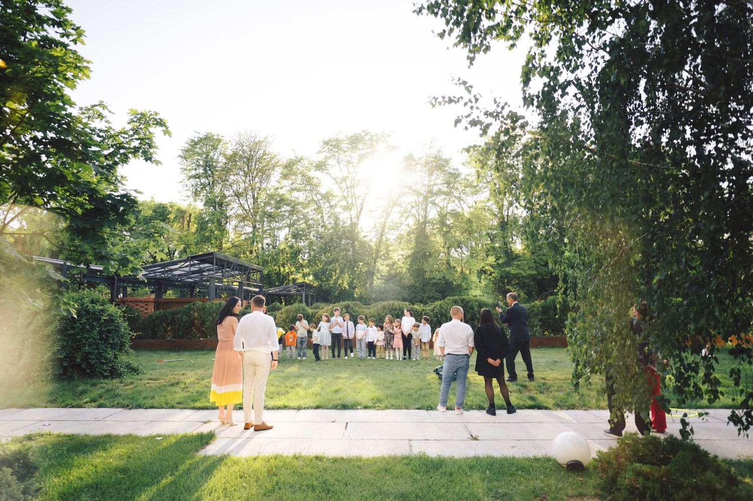 People enjoying an outdoor garden party with sunlight streaming through the trees.