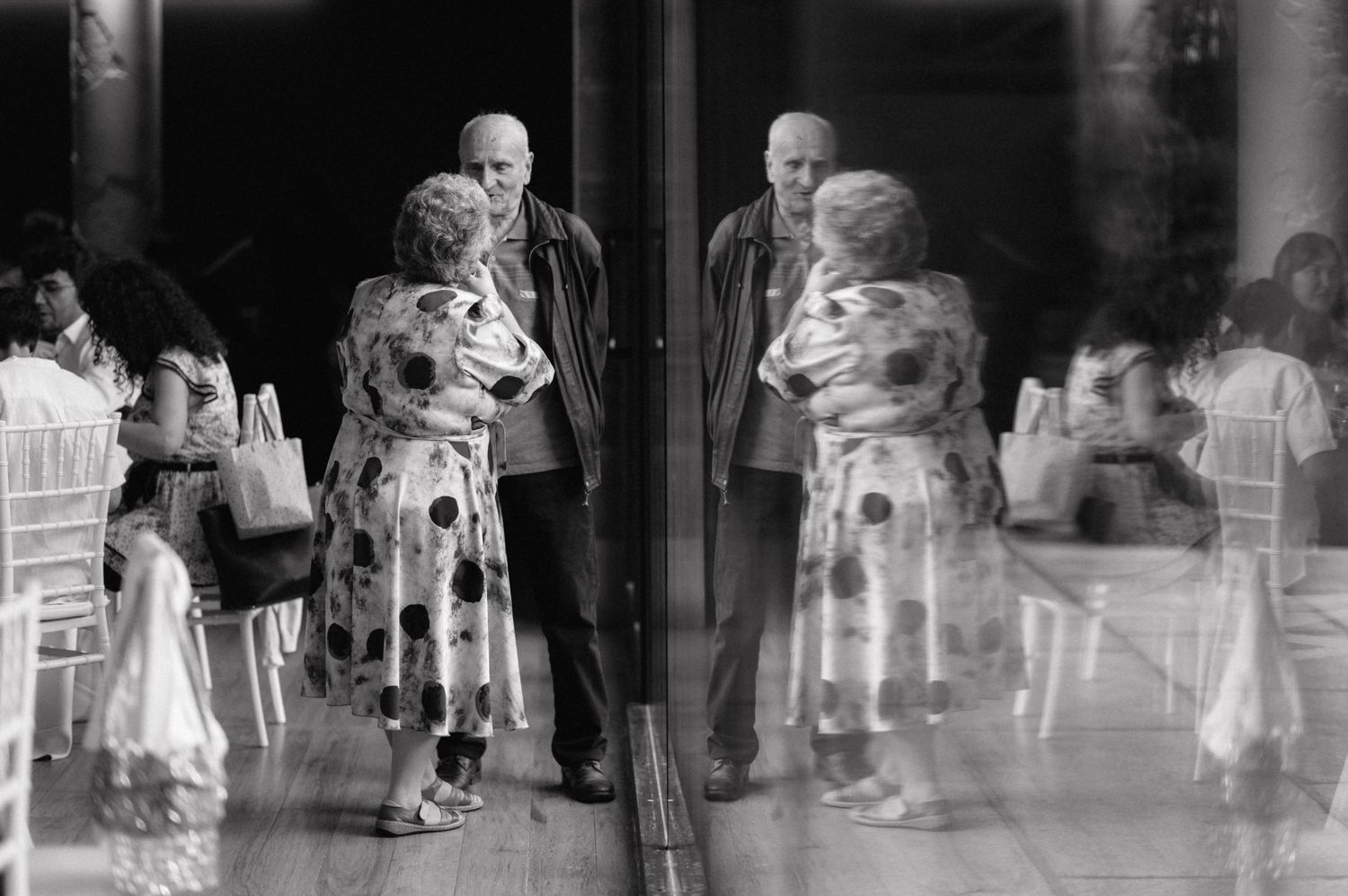A black and white artistic multiple exposure photograph showing ghostly figures dancing at an elegant social gathering.
