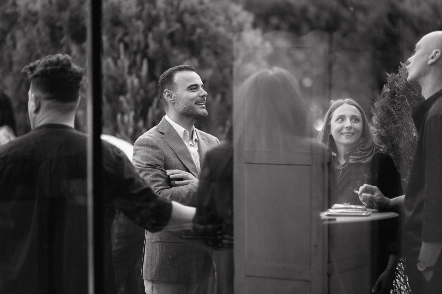 Black and white photograph of people engaged in conversation at what appears to be an outdoor social gathering.