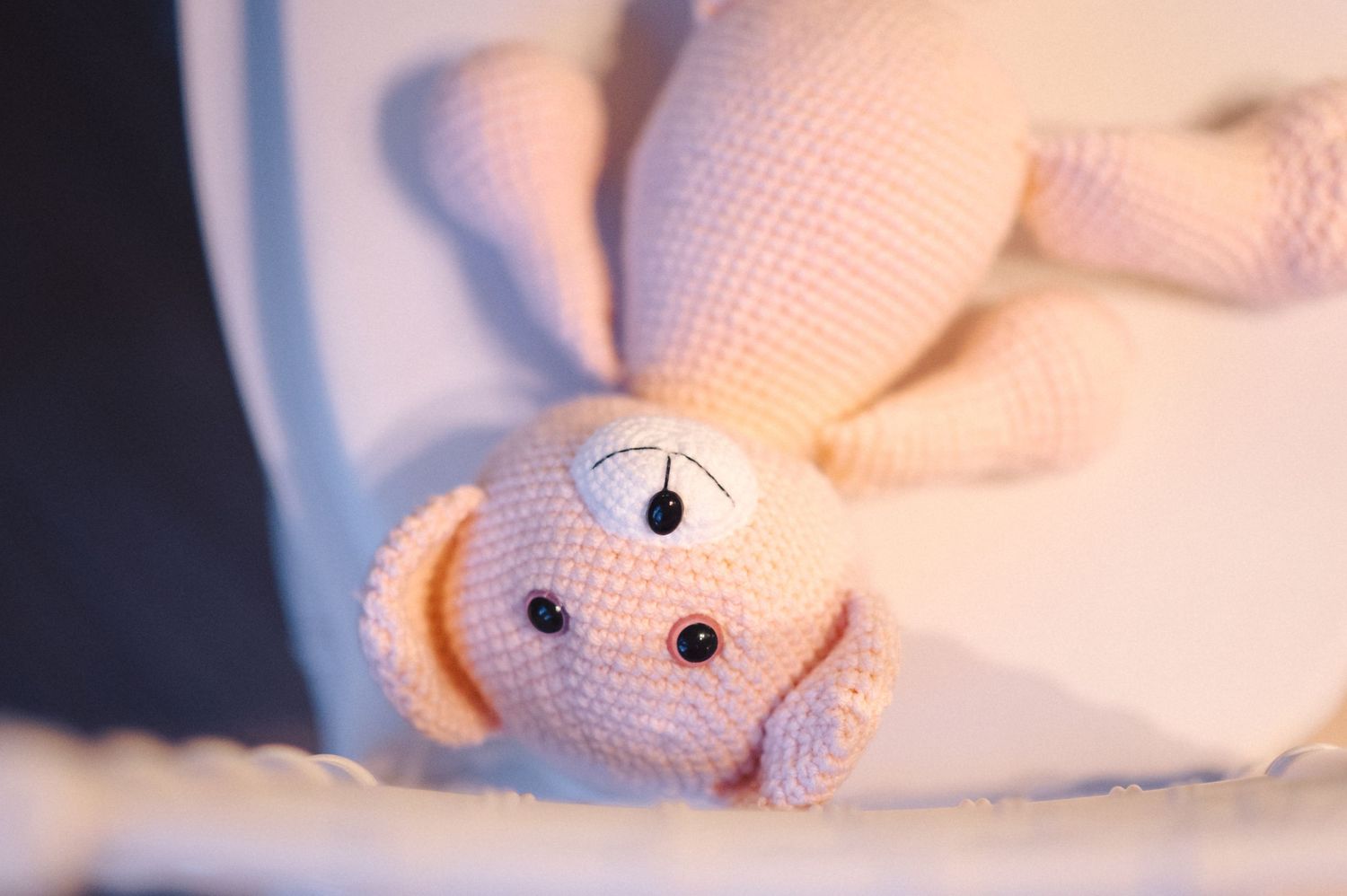 A close-up view of a pink amigurumi toy with embroidered facial features against a blurry background.