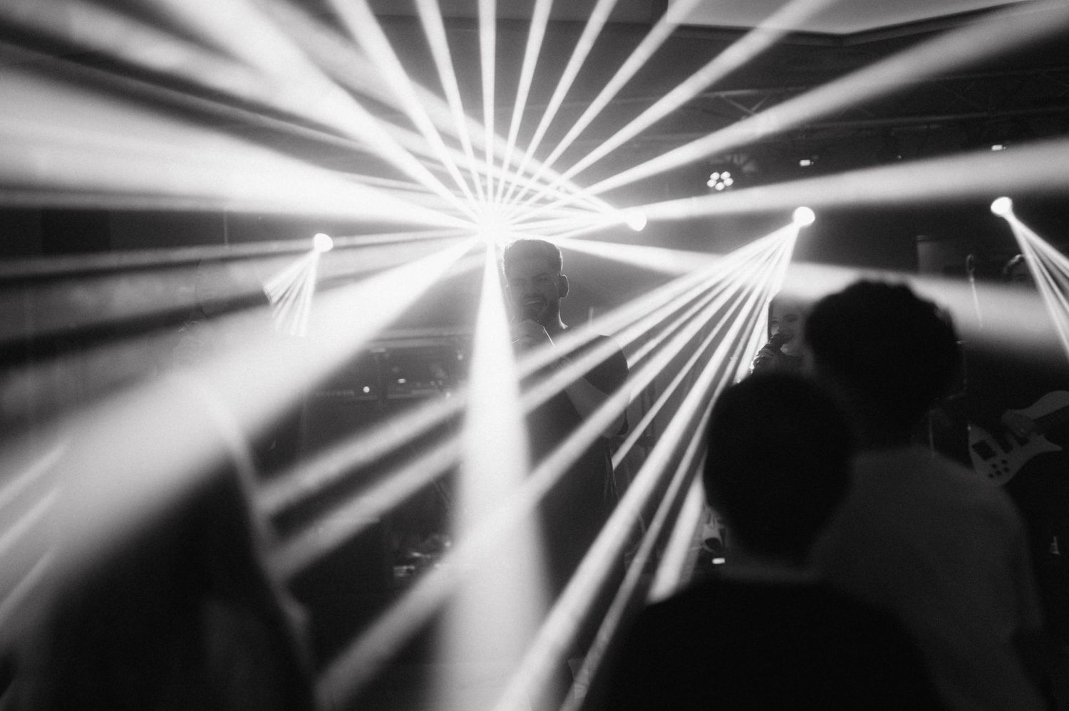 Dramatic white light beams pierce through darkness at a nightclub or concert venue creating an atmospheric display.