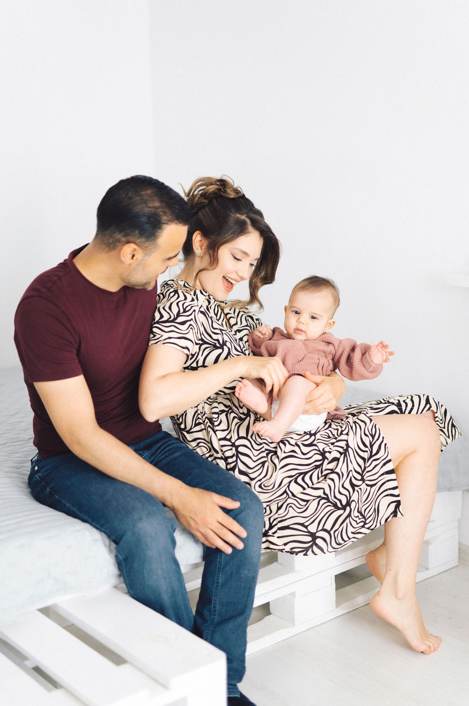 A family sitting together on white wooden pallets in a bright room.
