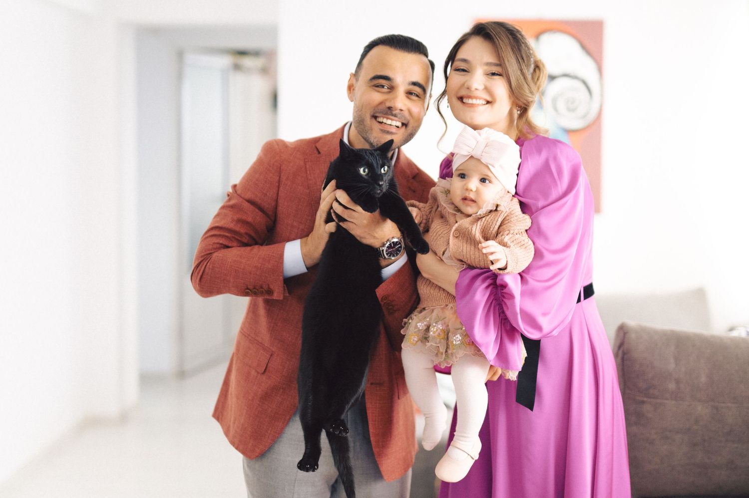 A couple smiles while holding a black puppy and small dog in a bright indoor setting.