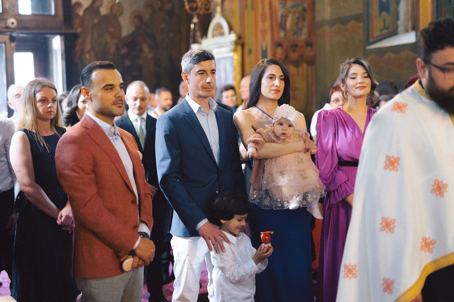 A group of formally dressed people stand together during an Orthodox Christian church ceremony.