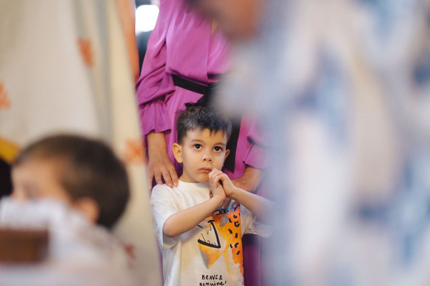 A young child in a white t-shirt is seen looking upward while someone in purple clothing stands behind them.