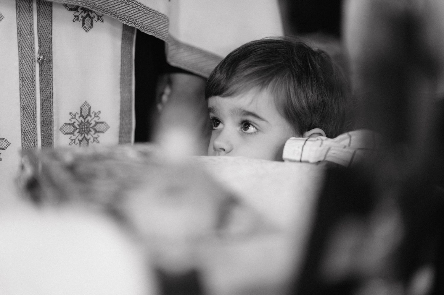 A black and white artistic photograph shows a small child peeking over a table or surface while looking to the side.