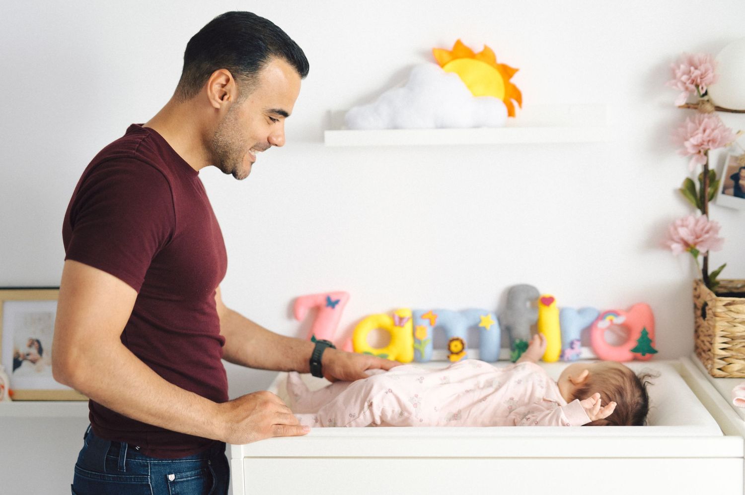 A parent changing a baby's diaper on a changing table with soft toys and decorations in the background.